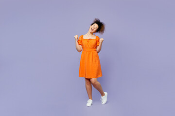 Full body young latin woman she wear orange blouse casual clothes doing winner gesture celebrate clenching fists say yes isolated on plain pastel purple background studio portrait. Lifestyle concept.