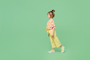 Full body side view smiling happy little child kid girl 6-7 years old wear casual clothes walk go isolated on plain pastel green background studio portrait. Mother's Day love family lifestyle concept.