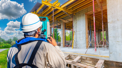 Man surveyor. Home construction. Guy with geodetic instrument. Surveyor with his back to camera. Worker uses optical theodolite. Surveyor near building under construction. Man builder at work.