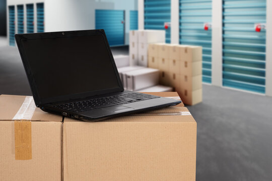 Warehouse business. Laptop on boxes. Parcel near storage units. Warehouse corridors. Doors to storage containers. Laptop for renting warehouse via internet. Boxes near storage units. 3d image