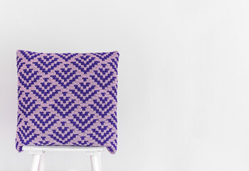 Handmade blue crochet pillow with abstract mosaic pattern on a chair against the white wall. Copy space.