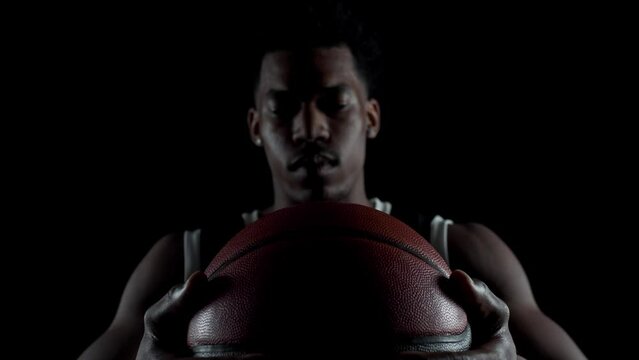 Basketball player sitting on a bench taking deep breath in. Concentrated african american sports man against black background.