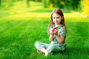happy baby girl in summer on the lawn with a red apple on the green grass and smiling, space for text