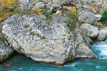 A mountain river with cold and clear water flows past a huge rock that fell from the top of the mountain. A mountain river with a greenish tint.
