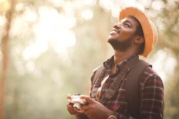 African travelers look at the natural beauty within the forest holding a camera to capture the...