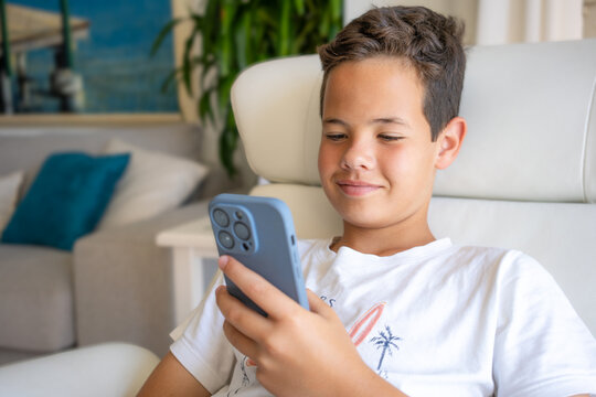 One preteen kid holding smartphone at home. Portrait face close up of a young boy using phone browsing social media sitting at staircase indoors