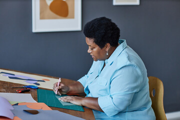 Side view of aged African American craftswoman working over new artwork while sitting by workplace...