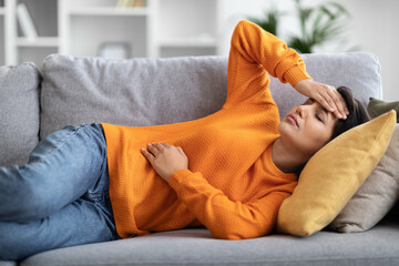 Unhealthy millennial indian lady lying on couch at home