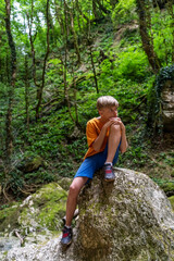 Naklejka na ściany i meble Contemplative boy sits on a moss-covered rock while relaxing in a mountainous area