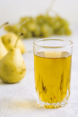 Juice of pears and grapes in a glass on a white wooden background
