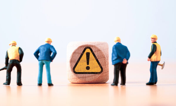 Miniature figure of senior engineer standing and see at warning exclamation caution sign for notification maintenance and dangerous sign area and safety first concept.