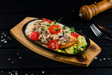 Braised pieces of pork with onions, cream, tomatoes, lettuce, spices and herbs in a cast-iron skillet.