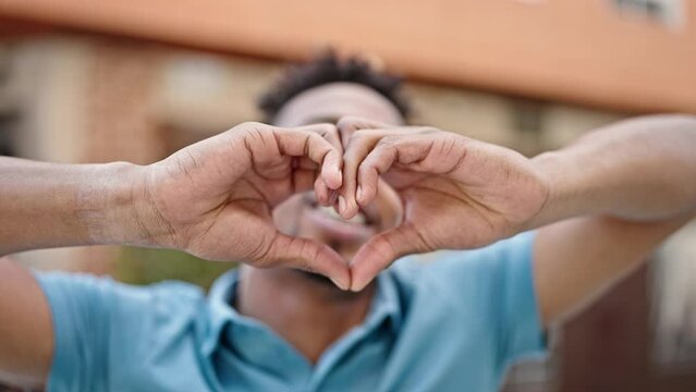 African american man doing heart gesture with hands dancing at coffee shop terrace