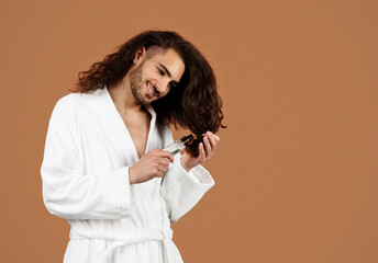 Young Man Applying Serum On Long Curly Hair, Brown Background