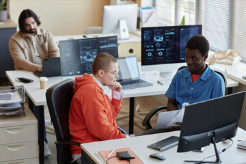 Young African American male manager with papers making report about cyber security points and rules to female colleague at meeting