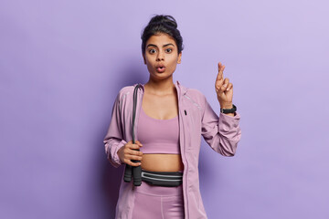 Fitness and sport concept. Surprised sporty young woman poses with skipping rope keeps fingers...