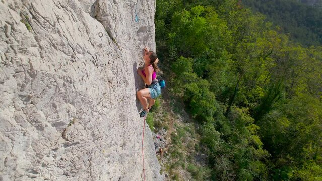 CLOSE UP: Sporty woman clips belay rope in quickdraw while she climbs rocky wall. She is advancing on a sharp end of rope along the climbing route in limestone wall. Amazing location for rock climbing