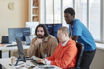 Obraz na płótnie Canvas Young businesswoman typing on computer keyboard while her two intercultural male colleagues looking at screen at working meeting