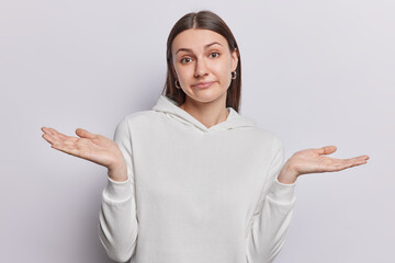 Clueless young dark haired woman has face filled with uncertainty spreads palms sideways cannot...