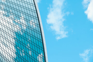 View of glass facade of skyscraper and blue sky with white clouds. Modern architecture, urban space. Abstract background.