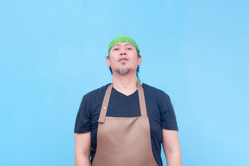 An expressionless middle-aged barista wearing brown apron standing straight. Isolated on a blue background.