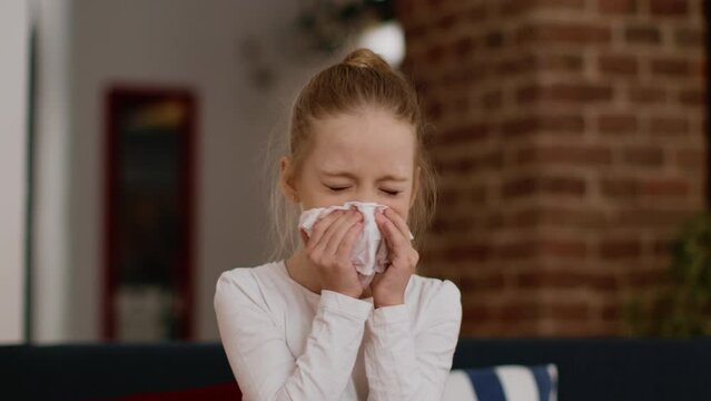 Kids and seasonal diseases. Portrait of sick little girl blowing her nose into paper tissue and coughing, free space