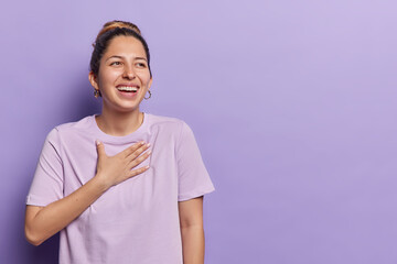 Horizontal shot of happy European woman smiling and laughing keeps hand on chest concentrated aside...