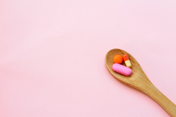 Top view variety of colorful vitamin and medicine pills in wooden spoon on pink background. Top...