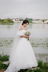 Young beautiful bride in a dress on shore of a lake outdoors. Happy wedding day of marriage....