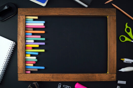 back to school blank blackboard, colorful chalks and stationery objects, education supplies on dark background