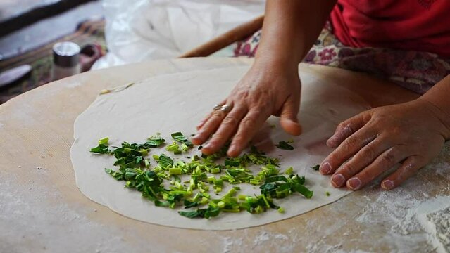 Hands of Turkish cook preparing potato, greens and cheese gozleme on wooden table. Traditional stuffed pancakes in Alanya, Turkey