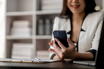 Beautiful asian woman looking at data on phone, businesswoman working in office attentively to grow and modernize start-up business, she is analyzing company's market and financial data.