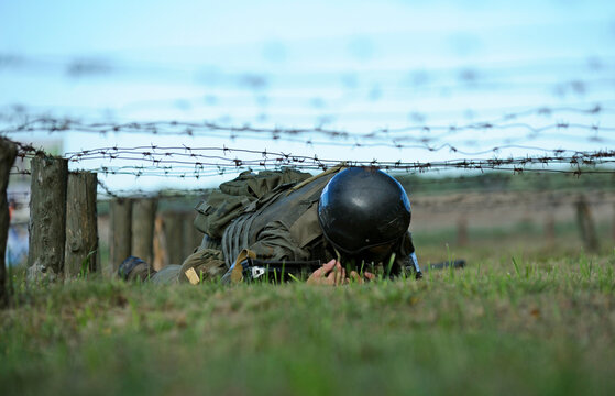 Fully equipped soldier crawling under barbed wires overcoming obstacle course. Ukraine