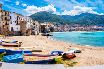 Fototapeta na wymiar Fishing boats on beach of Cefalu, medieval town on Sicily island, Italy. Seashore village with historic buildings, clear turquoise sea water and mountains. Popular tourist attraction near Palermo