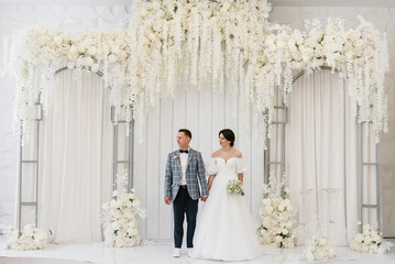 Bride and groom get married. Newlyweds with a bouquet,  standing on wedding ceremony under arch...