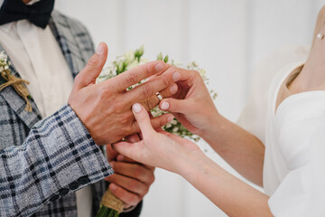 Engagement closeup. Marriage. Newlyweds stands on wedding ceremony under arch decorated white flowers. Bride and groom getting married and wear wedding rings. Woman and man while ceremony. Vows
