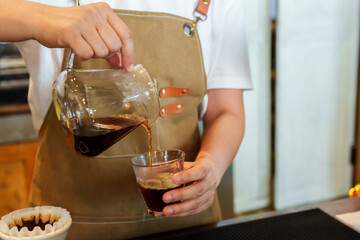 Close-up barista hand in cafe bakery with, lift glass cup that is used filter for, pour into clear glass coffee mug, It is freshly brewed coffee, drink after brew is finished enjoy aroma taste coffee.