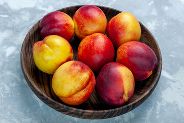 Fototapeta na wymiar front close view fresh peaches mellow and tasty fruits inside brown plate on light-white desk fresh fruit mellow photo vitamine