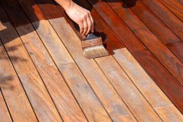 Ipe deck refreshing, worker's hand is oiling terrace decking with a painting brush - obrazy, fototapety, plakaty