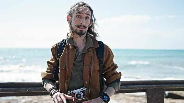 Young hispanic man tourist wearing backpack speaking at seaside