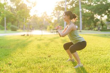 Female jogger. Fit young Asian woman with green sportswear squatting in park before running and...