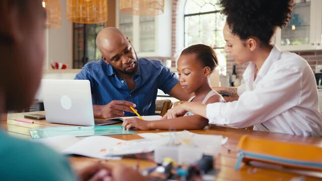 Family around table at home using laptop with parents helping children with STEM based homework on electronics project - shot in slow motion
