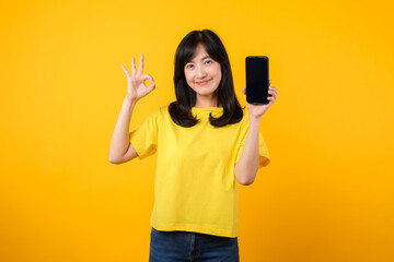 positive portrait young Asian woman wearing yellow t-shirt and denim jeans showing happy smile while showing smartphone screen and making the okay hand sign gesture. recommended applications concept.