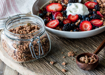 A jar filled with protein granola clusters and a breakfast bowl in behind.