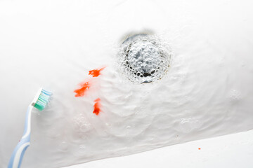 Toothbrush in a white washbasin with blood. Problem with gums.
