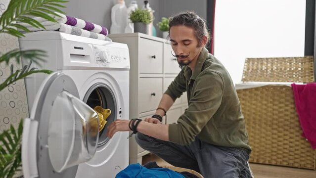 Young hispanic man washing clothes at laundry room