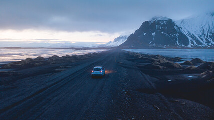 Une voiture sur un chemin rocheux avec des montagnes et un coucher de soleil en arrière plan. 
