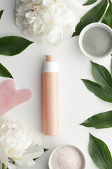 Obraz na płótnie Canvas Cosmetic beige tube from above overhead top view on white background in the frame of flowers, green leaves, pink quartz jade stone for massage, blue clay, blank mockup for your branding or packaging