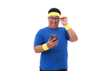 Happy Asian overweight man in sportswear standing while holding a cell phone. Isolated on white