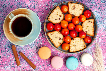 top view delicious sliced cake with sour fresh plums macarons and cup of tea on the pink desk pie sweet bake biscuit cookie sugar fruit